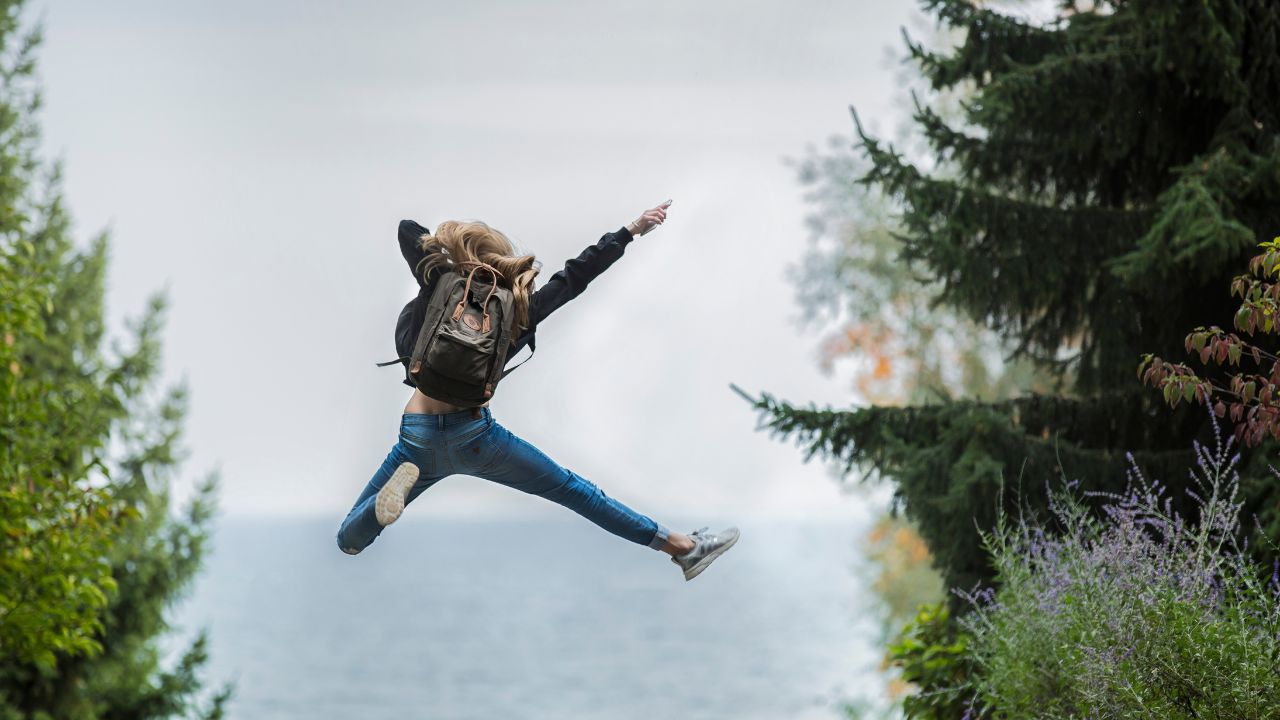 woman with a backpack jumping into the air