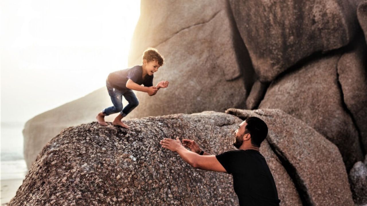 Child jumping off a rock into his dad's arms.