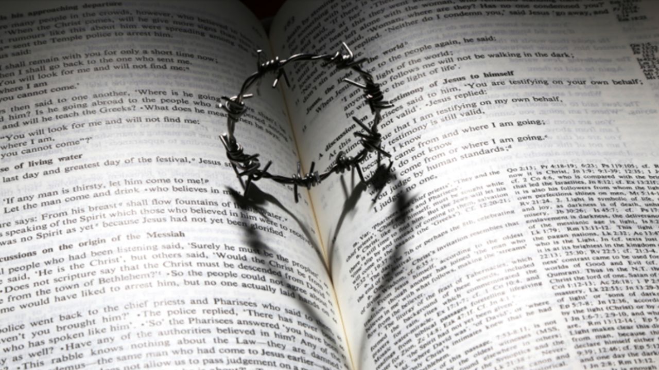 Bible with a crown of thorns casting a heart shaped shadow onto the pages